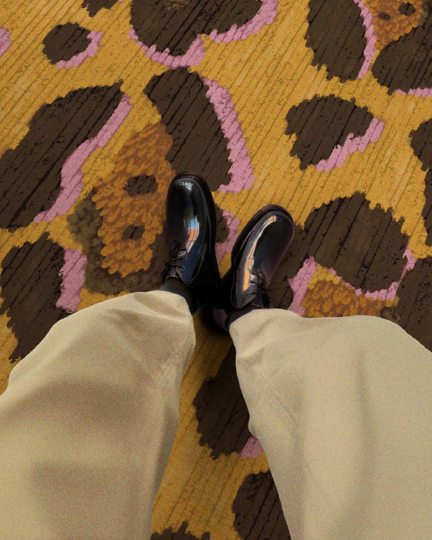 The man is wearing khaki pants and black leather shoes, relaxing on a colorful retro leopard area rug in yellow and brown hues.