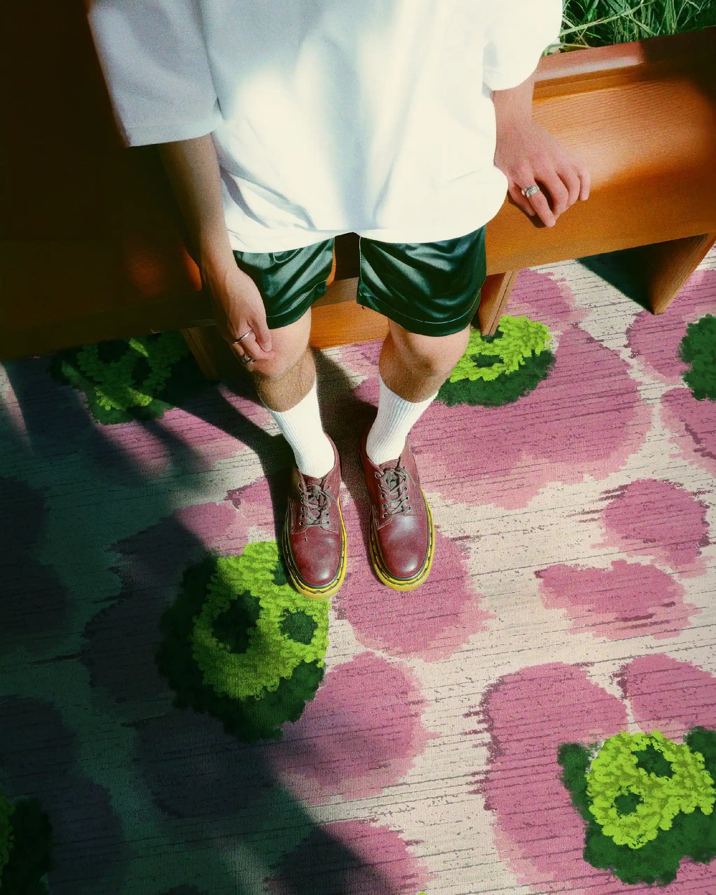A man wearing a white tee and dark green shorts stands on the eclectic floral area rug with cute leopard designs in pink and green hues in a cozy living room.