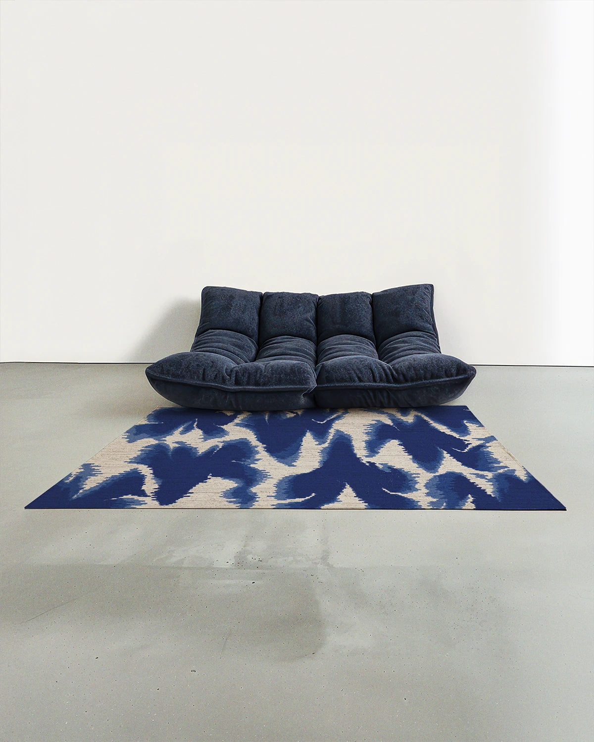 The blue and white aura mid century modern area rug 5x7 placed in a Scandinavian studio with a navy Togo sofa.