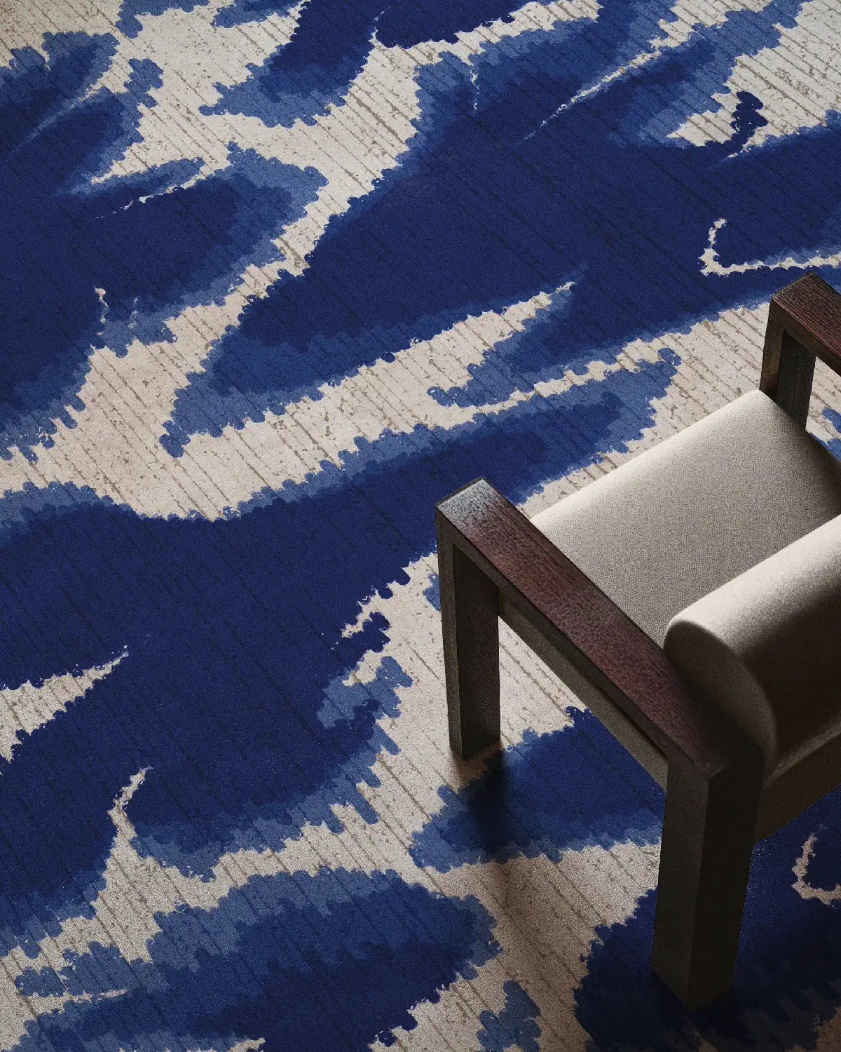 Mid century modern area rug placed underneath beige chair featuring abstract aura design in blue and white hues in modern living room.