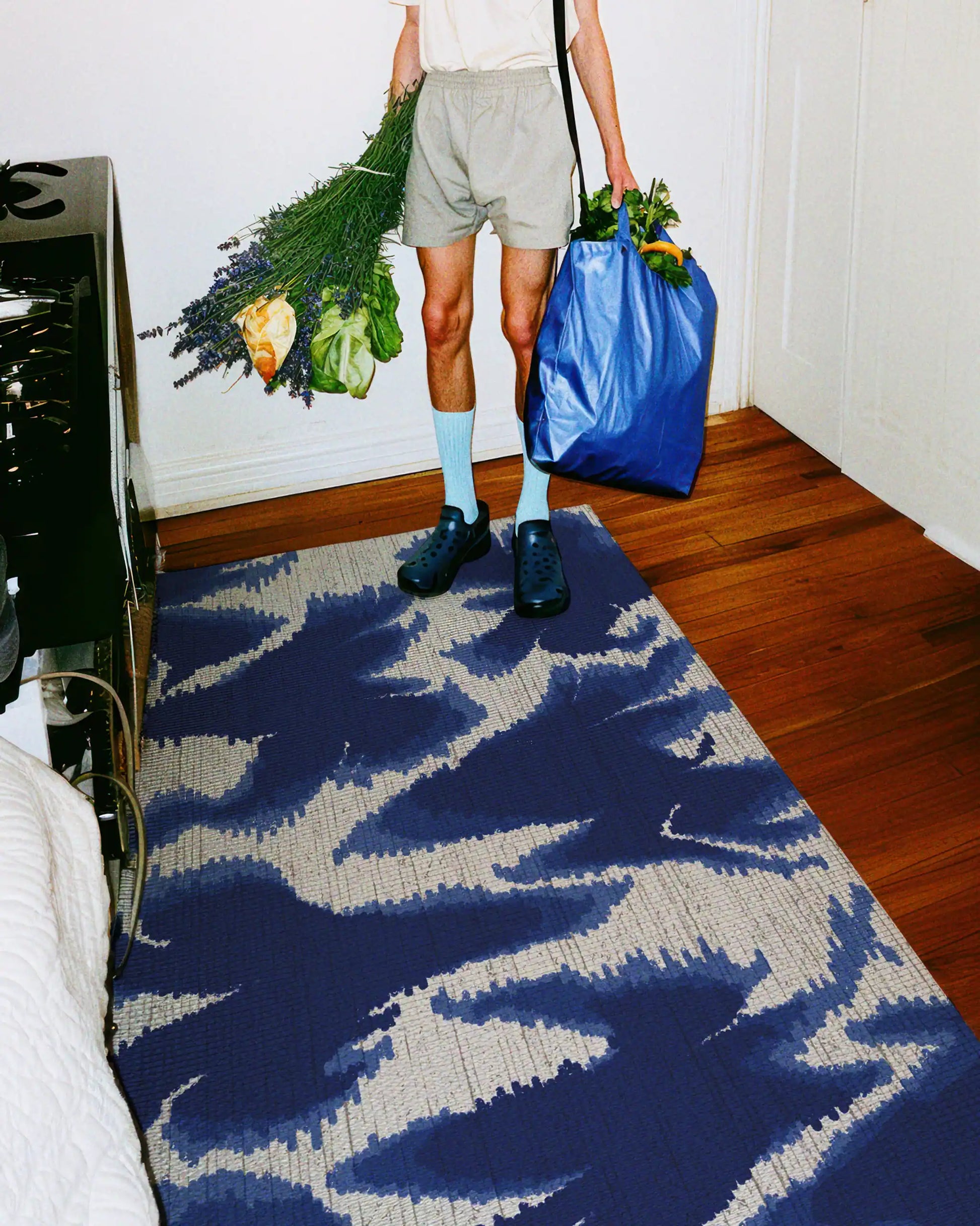 A man holding a blue shopping bag and flowers stands on a mid century modern area rug 4x6 with aura fish pattern designs in Klein blue and white hues in the kitchen.