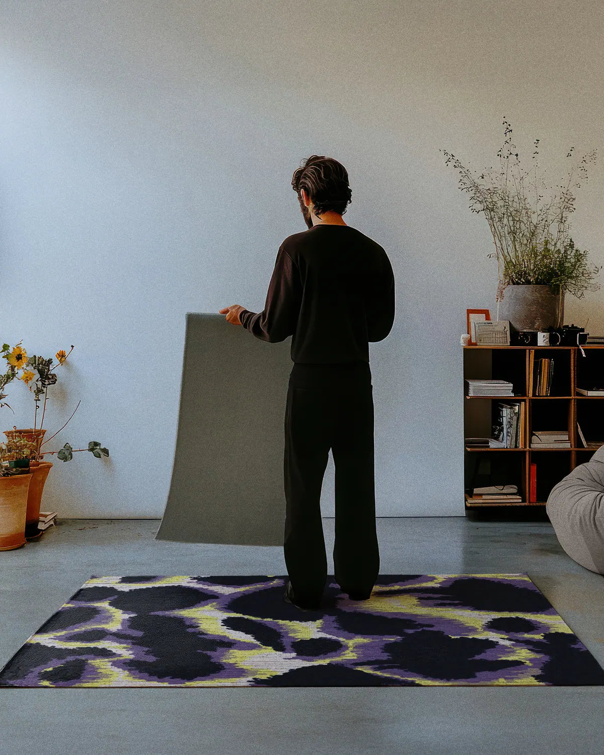 A man dressed in all black stands on a abstract cowhide rug 4x6, showing the nonskid rug backing of a 2x3 rug in a studio.