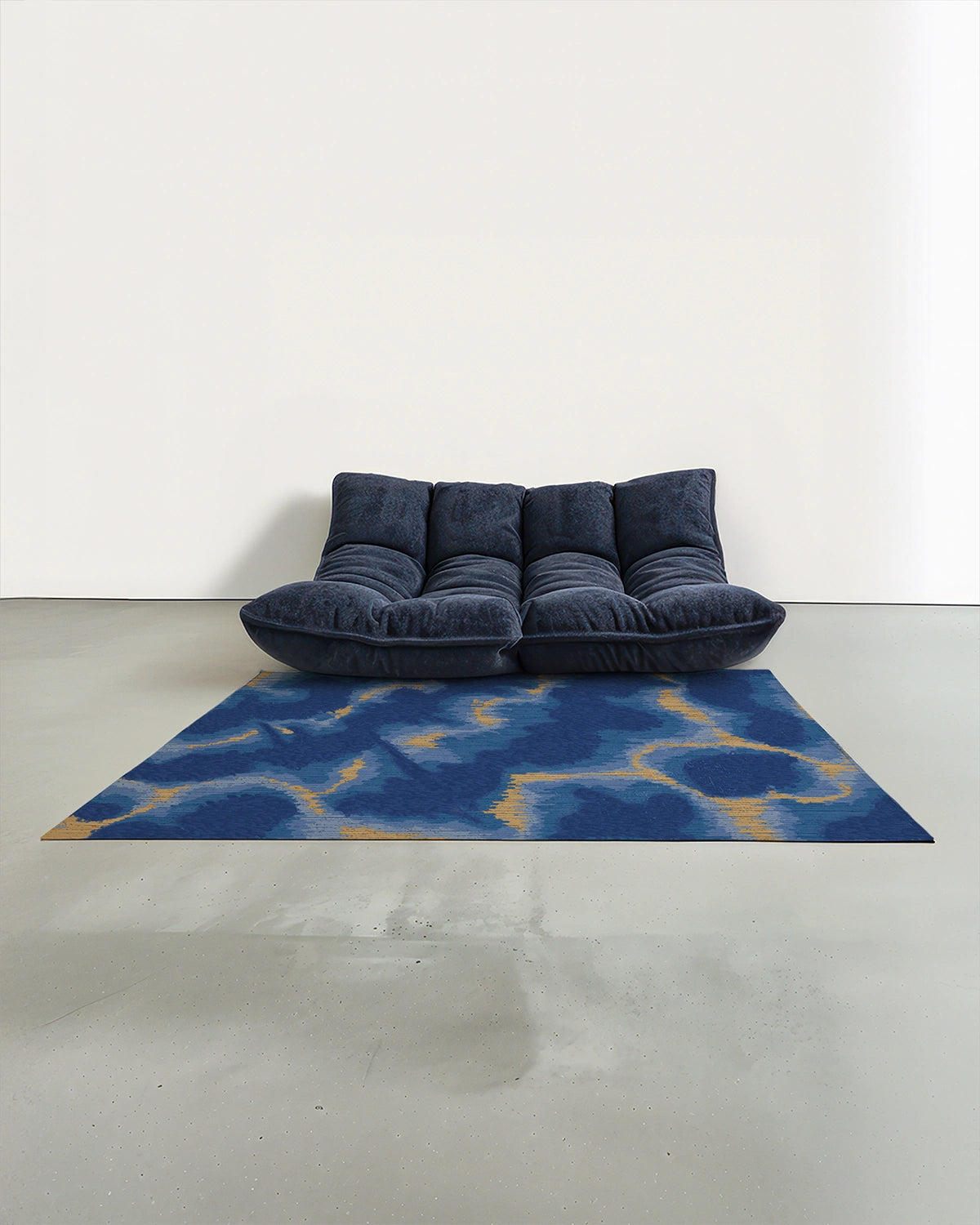 Abstract colorful area rug in Klein blue and sand beige aura design placed in a mid century modern studio with a navy Togo sofa.