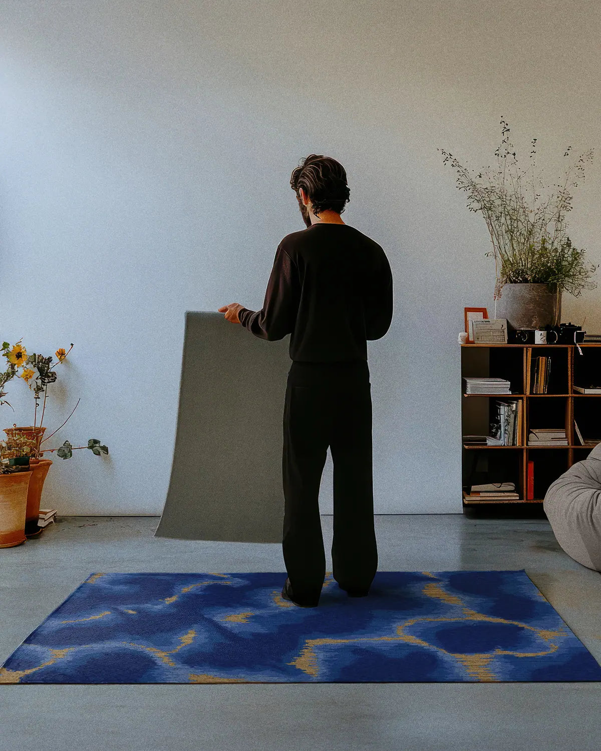 A man dressed in all black stands on a modern abstract area rug 4x6, showing the nonskid rug backing of a 2x3 rug in a studio.