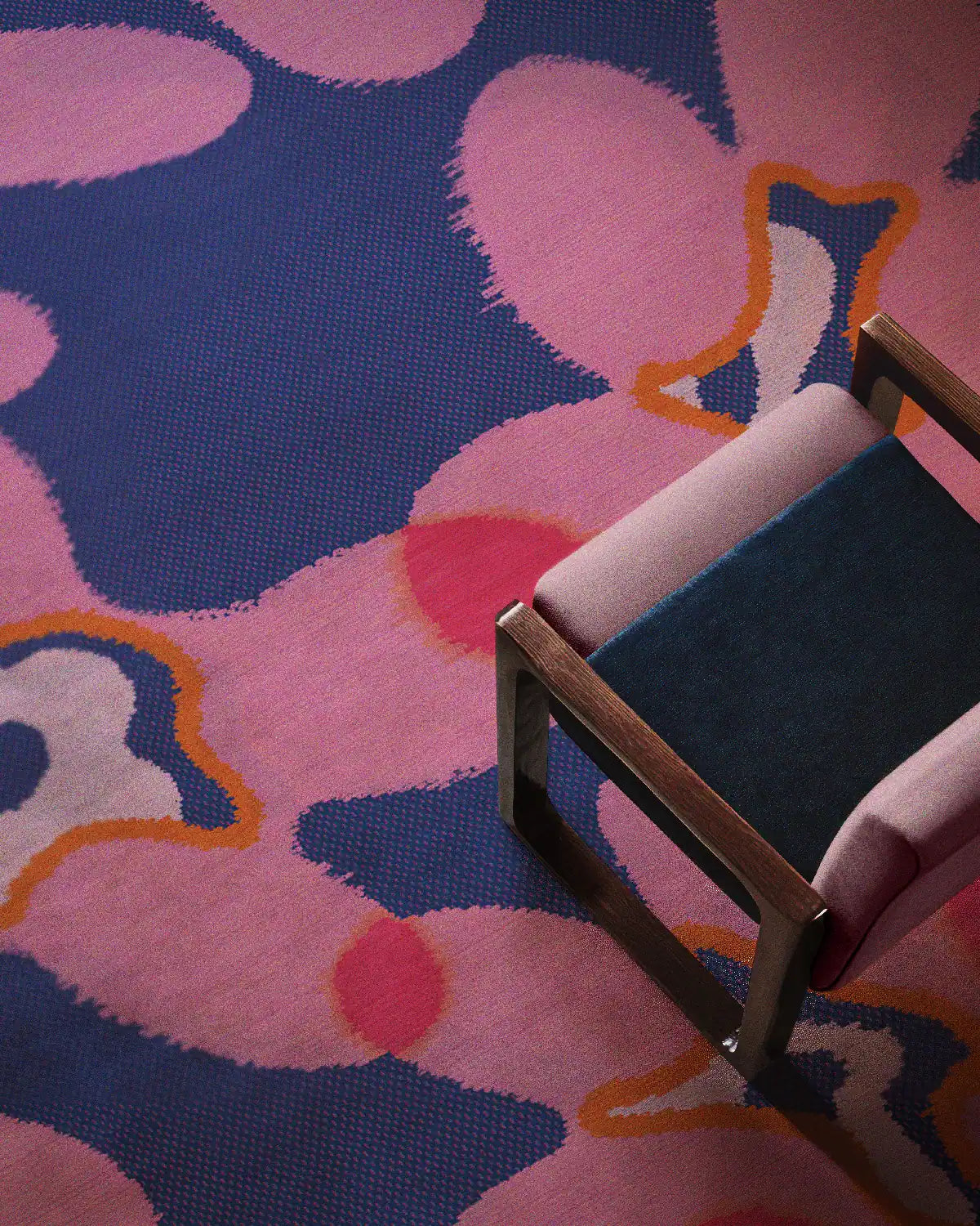 Overhead shot, the eclectic home decor features a floral area rug in hot pink and dark navy blue hues, placed underneath a pink wooden armchair in the living room.