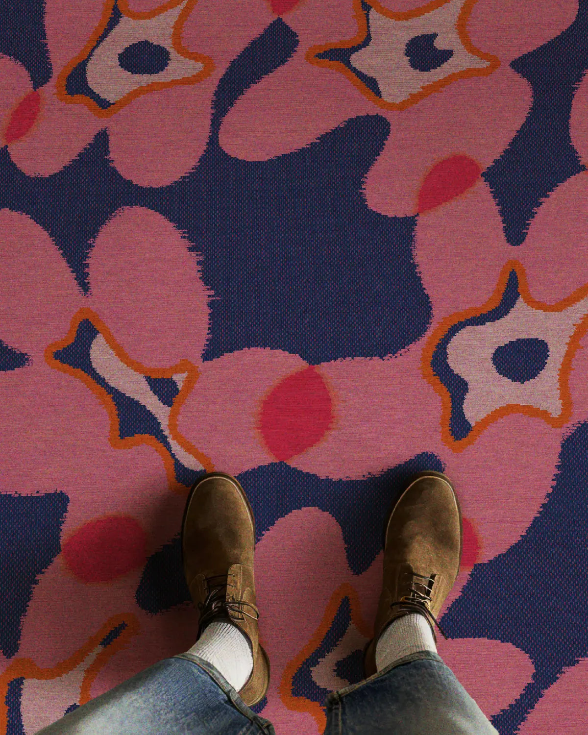 A man in trendy jeans and suede shoes stands on a cute floral area rug featuring abstract flower patterns in hot pink and dark blue hues, radiating a modern vibe in a stylish setting.
