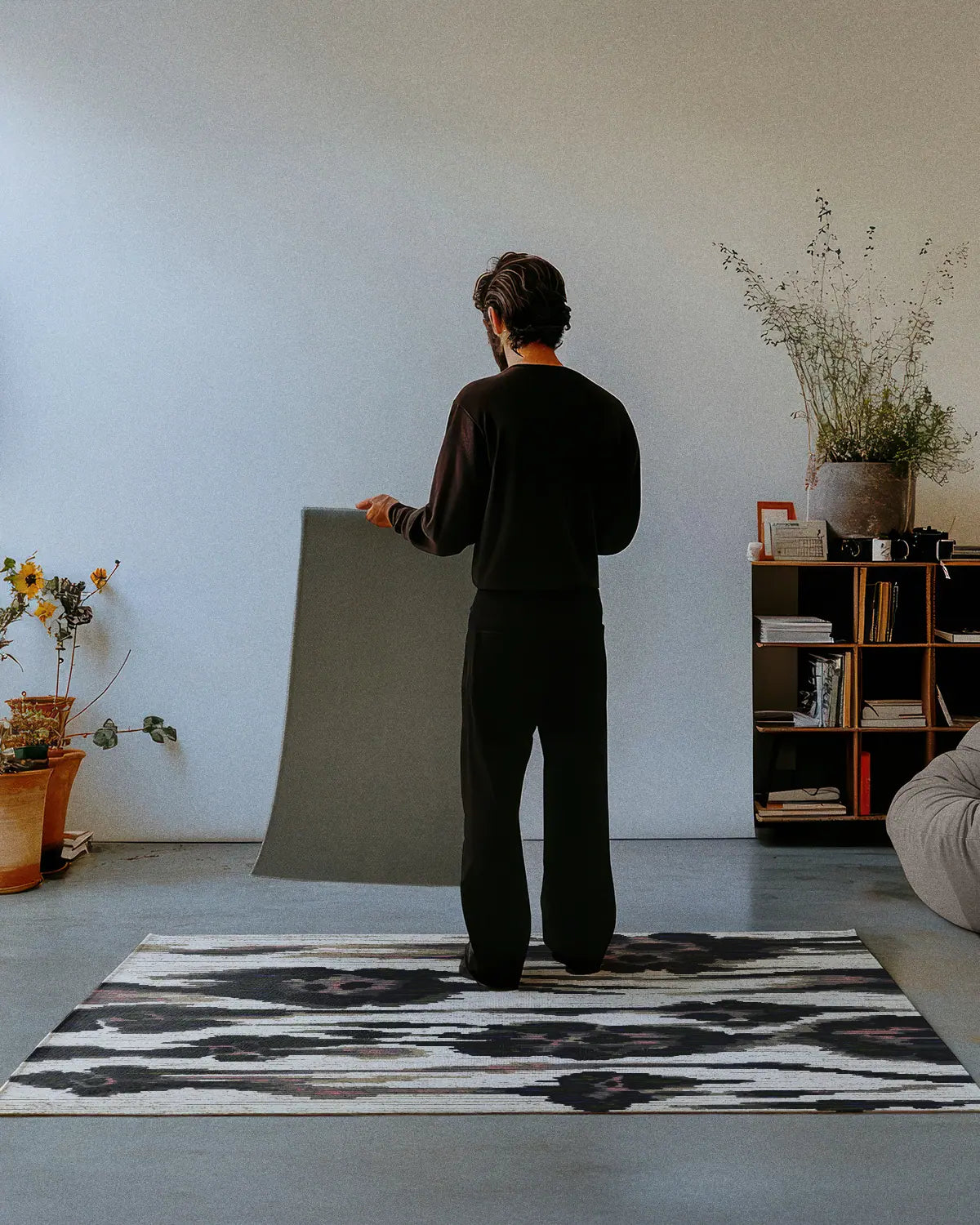 A man dressed in all black stands on an abstract animal print, leopard floral area rug 4x6, showing the nonskid rug backing of a 2x3 rug in a mid century modern studio.
