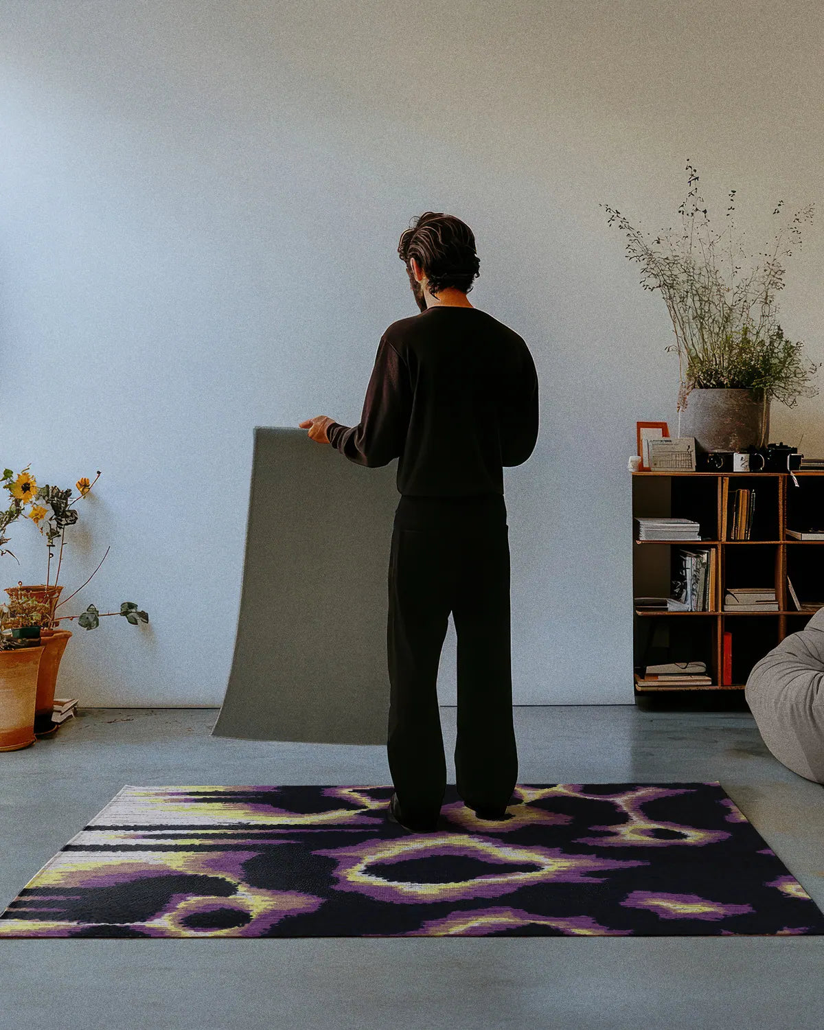 A man dressed in all black stands on a yellow leopard rug 4x6, showing the nonskid rug backing of a 2x3 rug in a studio.
