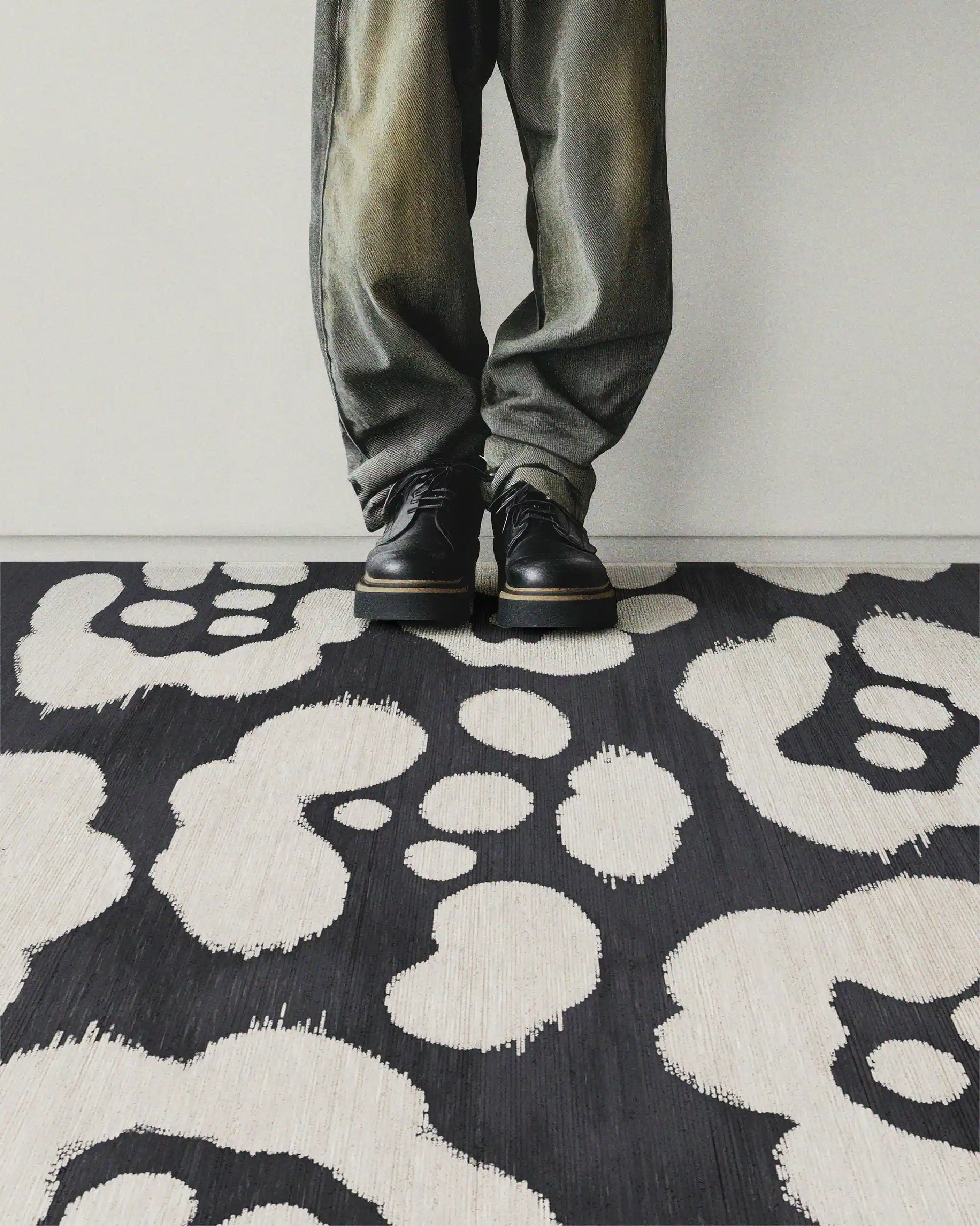 A man stands on black and white area rug featuring floral pattern, radiating a contemporary vibe in a stylish setting.
