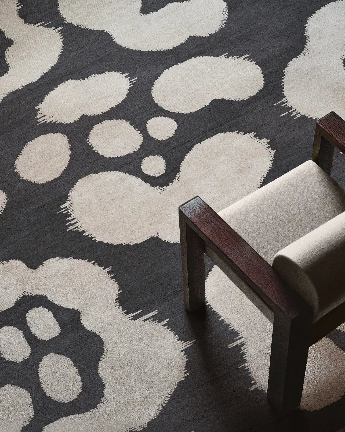 Black and white floral area rug is placed underneath a beige wood armchair for mid century modern apartment.