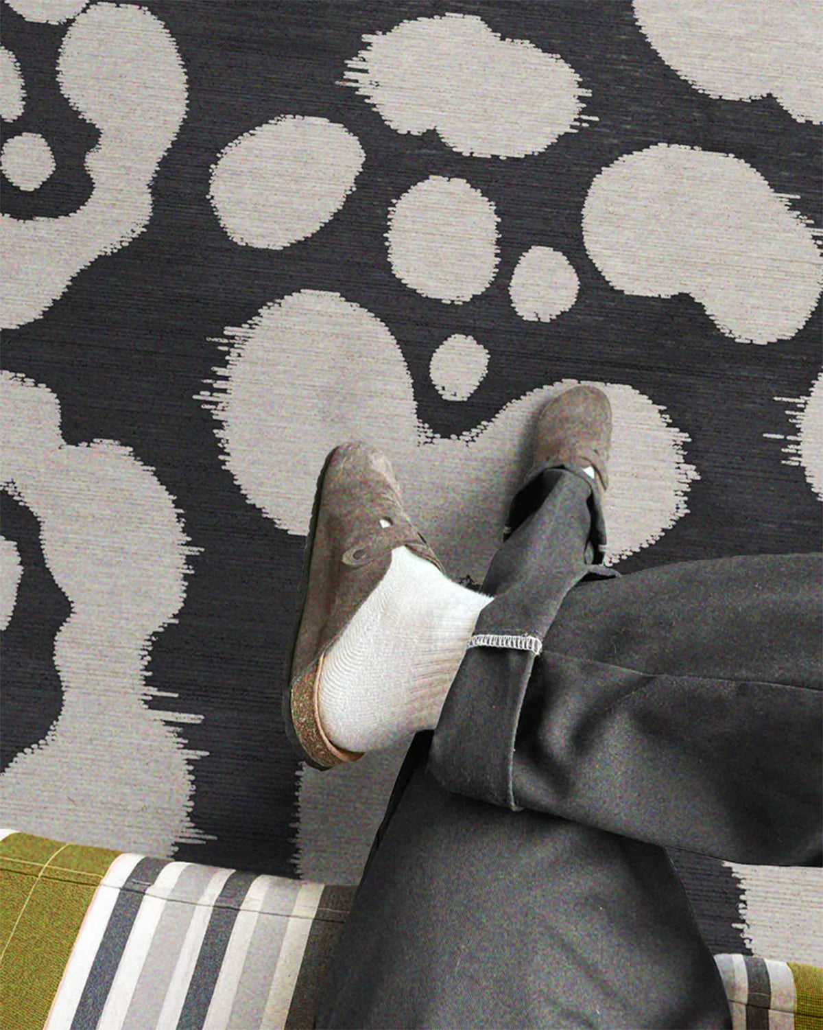 A man sits on the cozy bench in the yellow, grey, and white stripe pattern, relaxing one of his legs on a black and white flower area rug with cute floral pattern.
