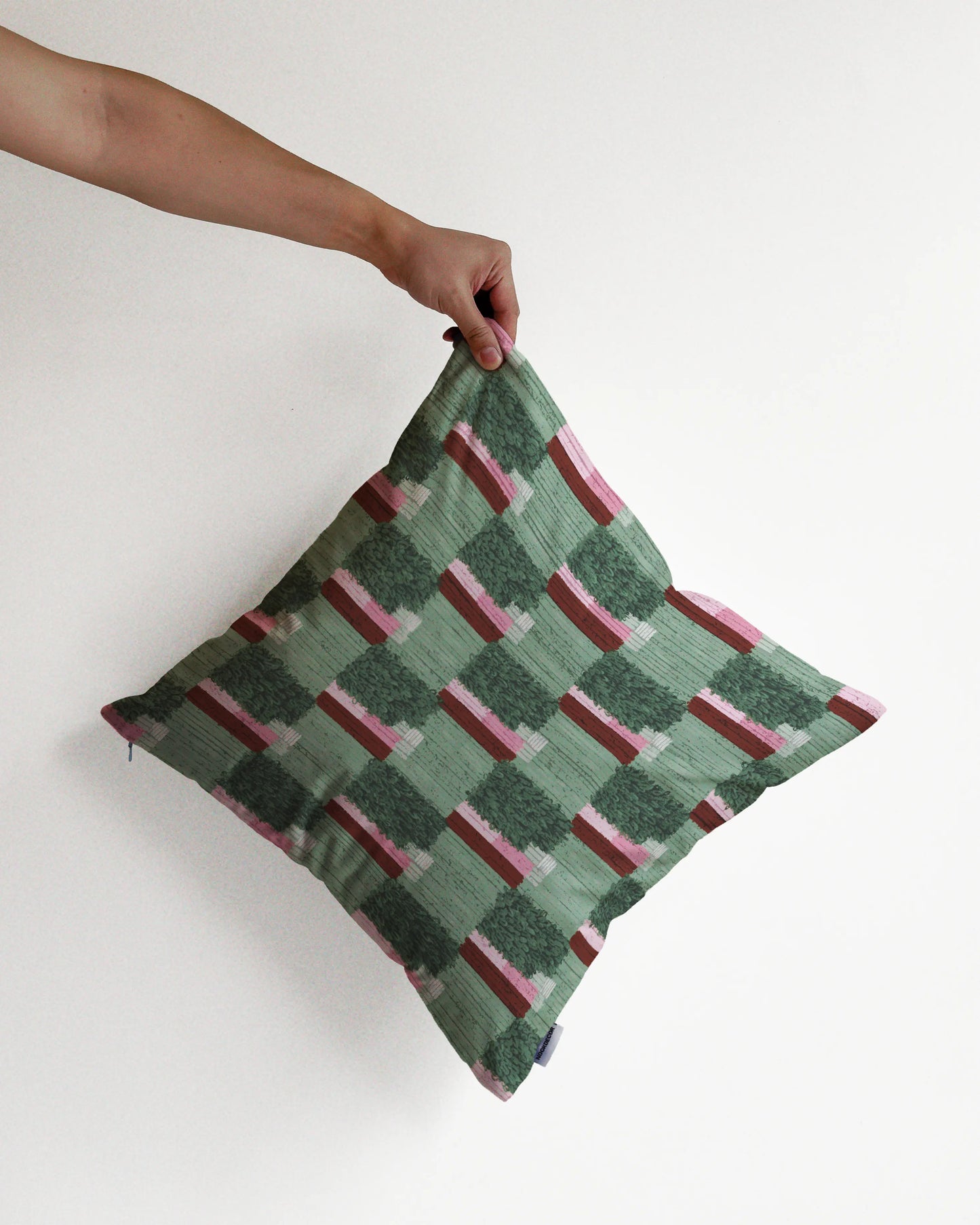 A hand holding an unique checkered cushion cover in sage, green and pink hues, against a minimalist beige background, perfect for eclectic dopamine decor in a modern apartment.