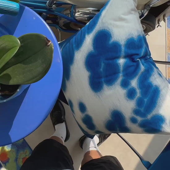 Product video of blue and white cushion cover placed on the blue chair with a colorful rug, and a vintage bicycle in NOOKDECOR's studio.