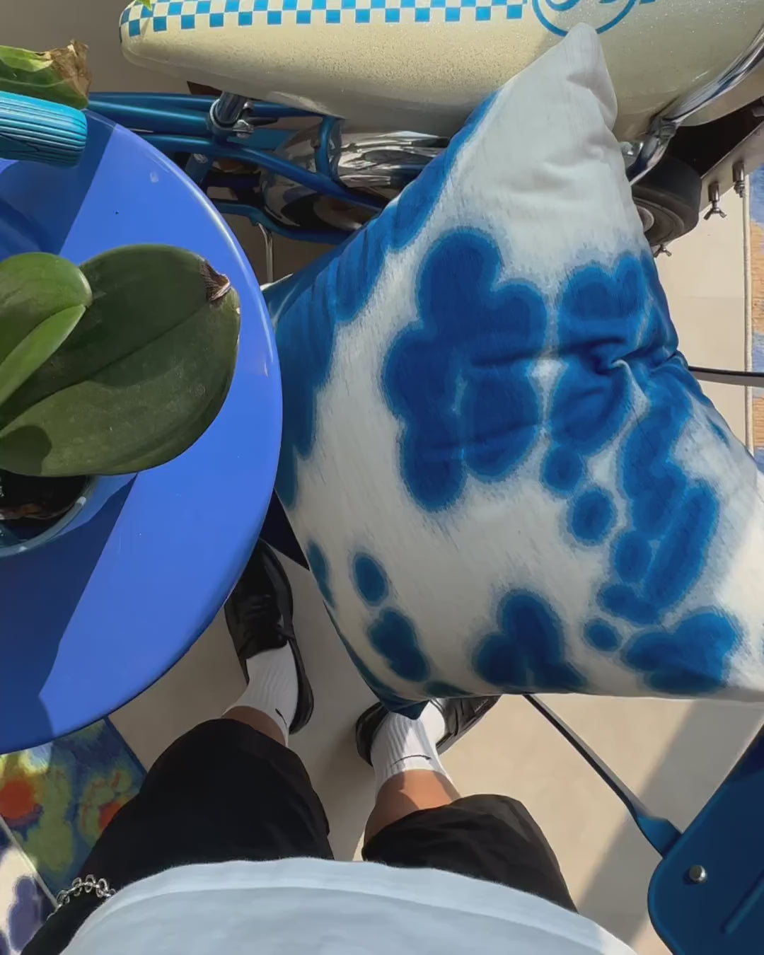 Product video of blue and white cushion cover placed on the blue chair with a colorful rug, and a vintage bicycle in NOOKDECOR's studio.