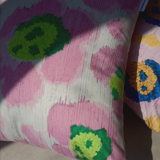 Product video of pink and green leopard cushion cover and purple and yellow throw pillow cover place on a textured floor in a studio. Dopamine home decor for maximalist apartment.