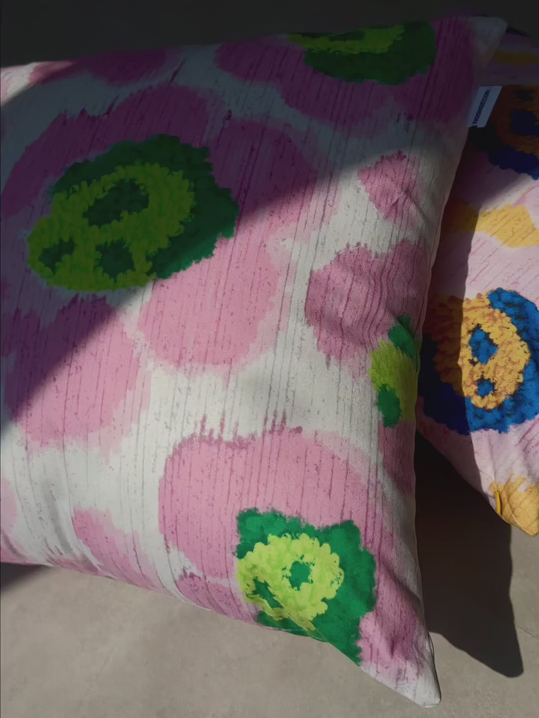 Product video of pink and green leopard cushion cover and purple and yellow throw pillow cover place on a textured floor in a studio. Dopamine home decor for maximalist apartment.