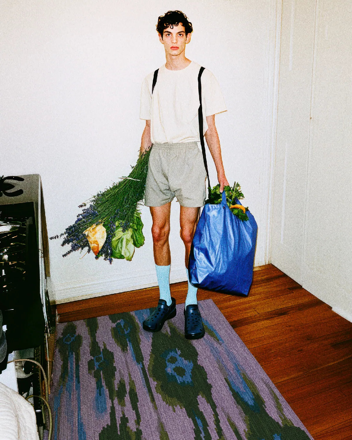 A man holding a blue shopping bag and flowers stands on a colorful area rug 4x6 with leopard designs in purple, blue, and green hues in the kitchen.